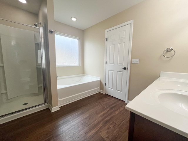 bathroom featuring a shower stall, a garden tub, double vanity, wood finished floors, and a sink