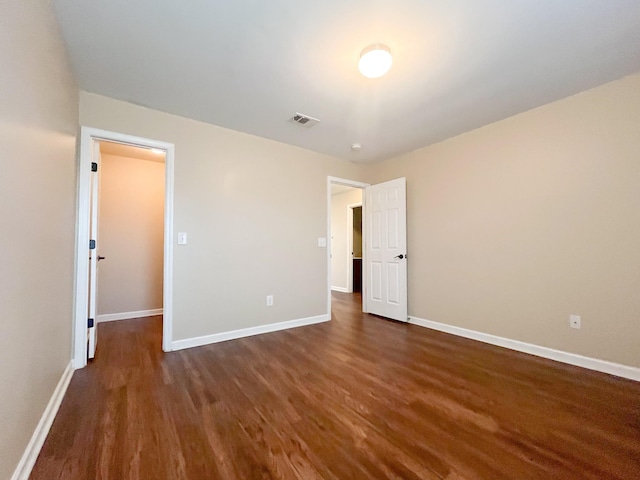 unfurnished bedroom with a spacious closet, baseboards, visible vents, and dark wood-style flooring