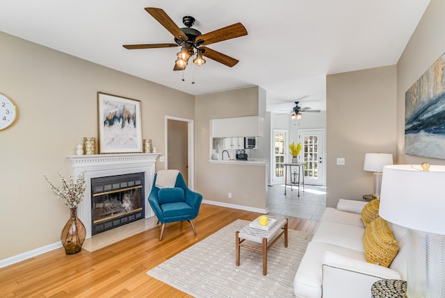 living room with a fireplace with flush hearth, baseboards, light wood-style floors, and a ceiling fan