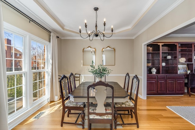 dining area featuring a chandelier, crown molding, light wood-style floors, and a tray ceiling