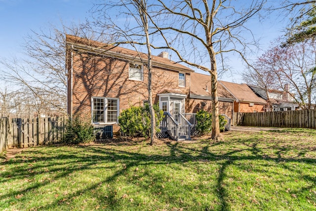 back of property with a yard, a fenced backyard, brick siding, and a chimney