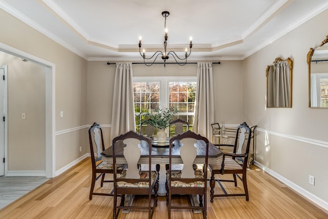 dining room featuring light wood-style floors, baseboards, a raised ceiling, and an inviting chandelier