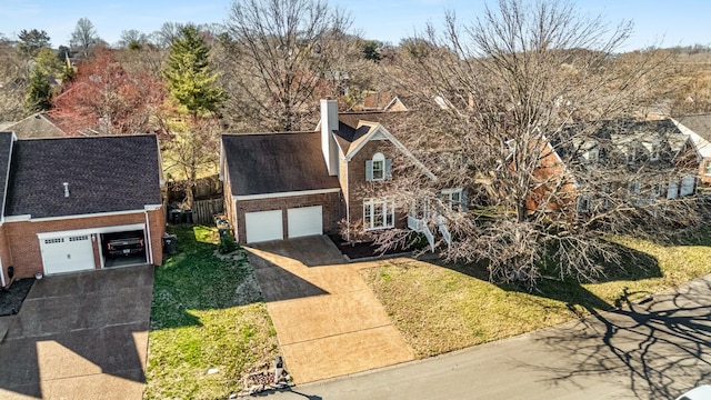 view of front facade with a front yard, a chimney, concrete driveway, a garage, and brick siding