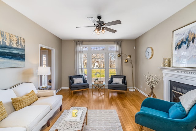 living area featuring a glass covered fireplace, wood finished floors, baseboards, and ceiling fan