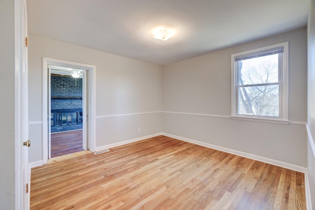 spare room featuring light wood-style flooring, a fireplace, visible vents, and baseboards