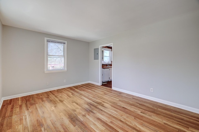 unfurnished room featuring electric panel, light wood-type flooring, baseboards, and a sink