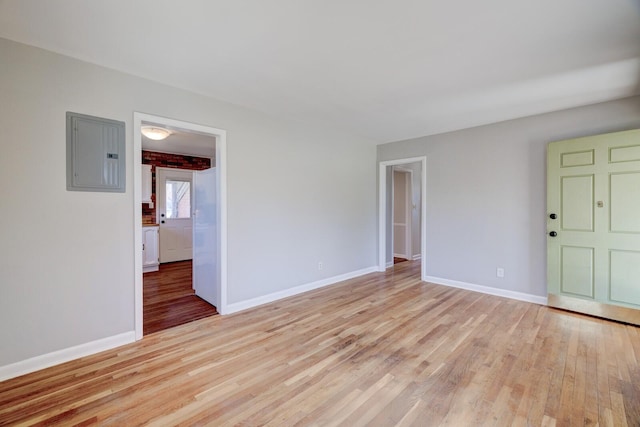 unfurnished room with electric panel, light wood-style floors, and baseboards