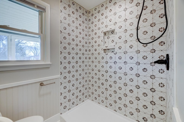 bathroom featuring a tile shower and a wainscoted wall