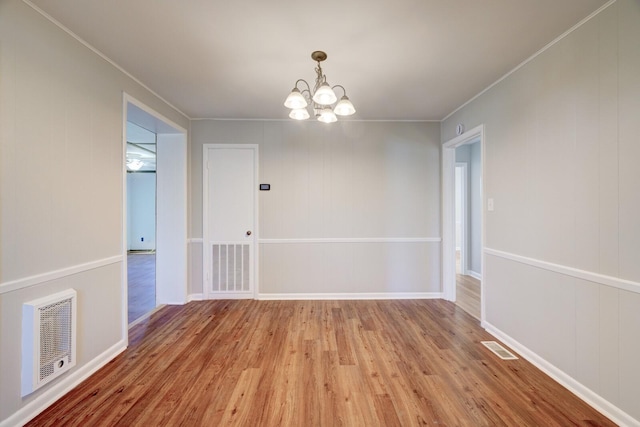 empty room featuring a notable chandelier, visible vents, crown molding, and wood finished floors