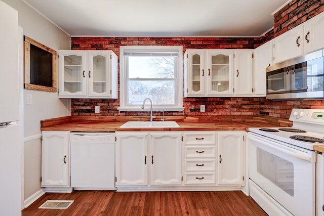 kitchen with visible vents, a sink, wood finished floors, white appliances, and white cabinets