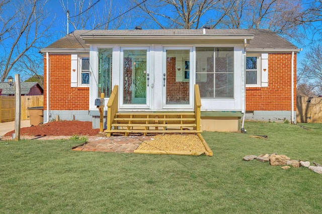 rear view of property with brick siding, a lawn, entry steps, and fence