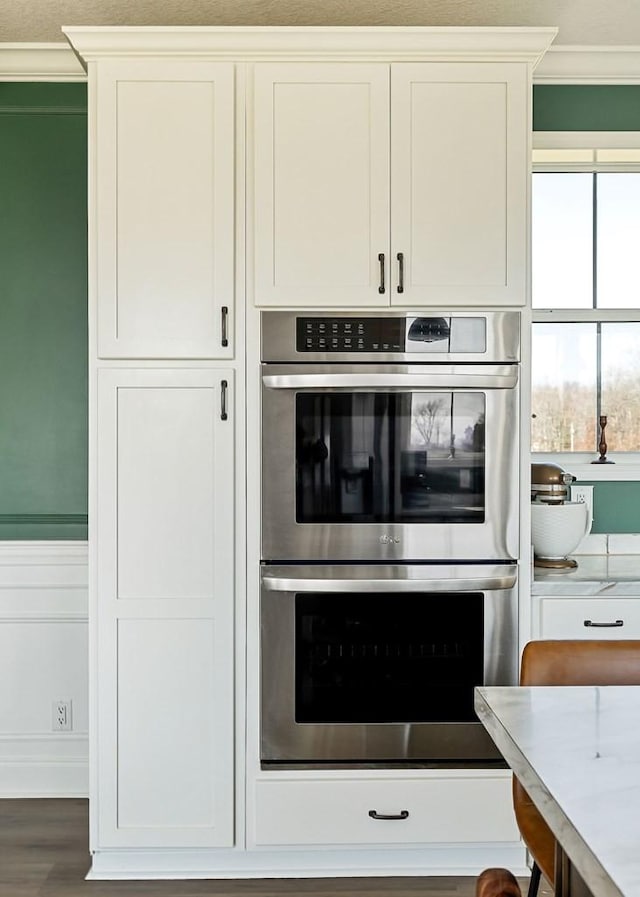 kitchen featuring double oven, white cabinets, crown molding, and light countertops