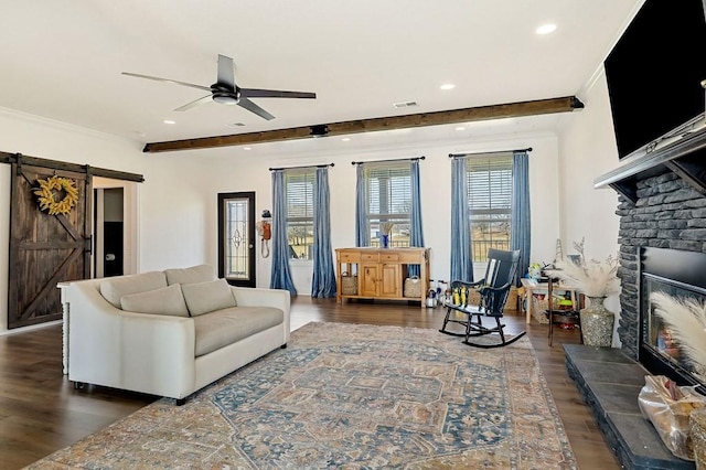 living room with a stone fireplace, a barn door, crown molding, and wood finished floors