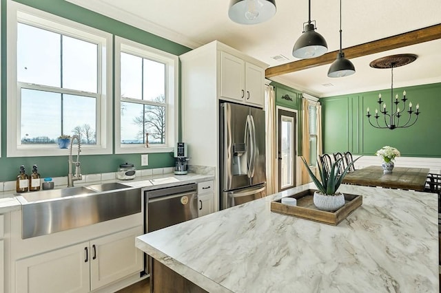 kitchen with a sink, stainless steel appliances, white cabinets, crown molding, and hanging light fixtures