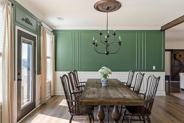 dining room with dark wood finished floors, crown molding, a decorative wall, and a chandelier