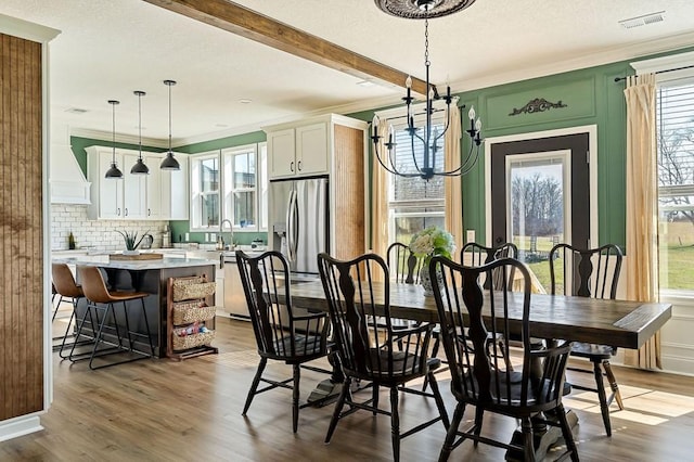 dining space featuring visible vents, crown molding, beamed ceiling, wood finished floors, and a textured ceiling