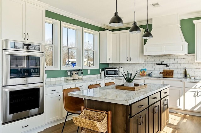 kitchen with visible vents, custom exhaust hood, ornamental molding, appliances with stainless steel finishes, and white cabinetry