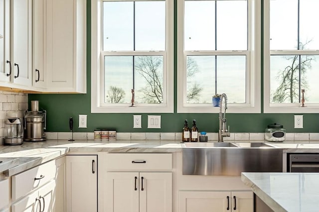 kitchen featuring white cabinetry, light stone counters, and a sink