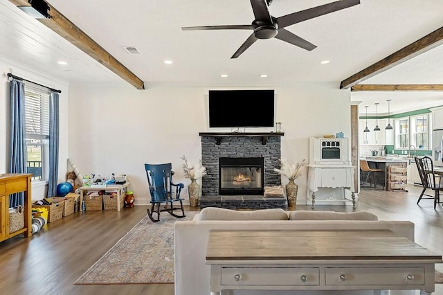 living room with a stone fireplace, beamed ceiling, wood finished floors, and visible vents