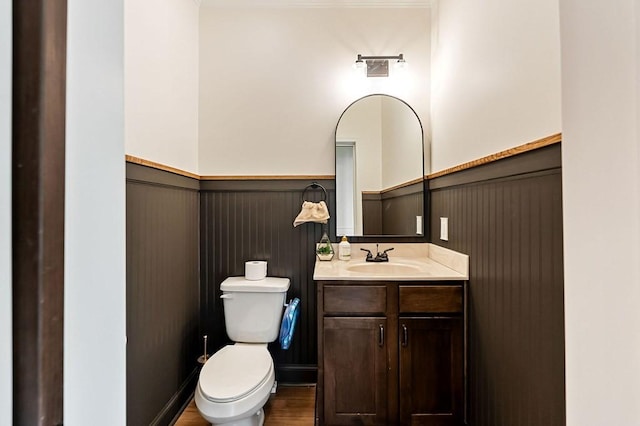 half bath featuring vanity, toilet, wood finished floors, and wainscoting