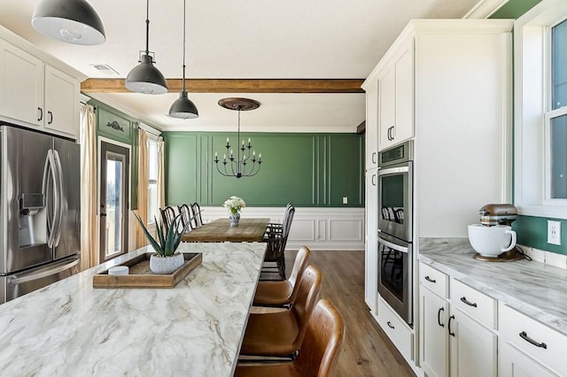 kitchen with stainless steel appliances, beam ceiling, white cabinets, and a decorative wall