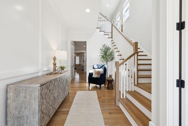 entryway with light wood-style flooring, ornamental molding, recessed lighting, a towering ceiling, and stairs