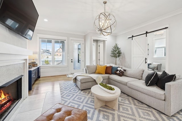 living room with ornamental molding, a barn door, a fireplace, light wood finished floors, and baseboards