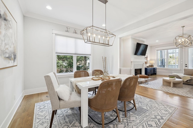 dining area featuring baseboards, light wood-style flooring, a fireplace, ornamental molding, and a notable chandelier