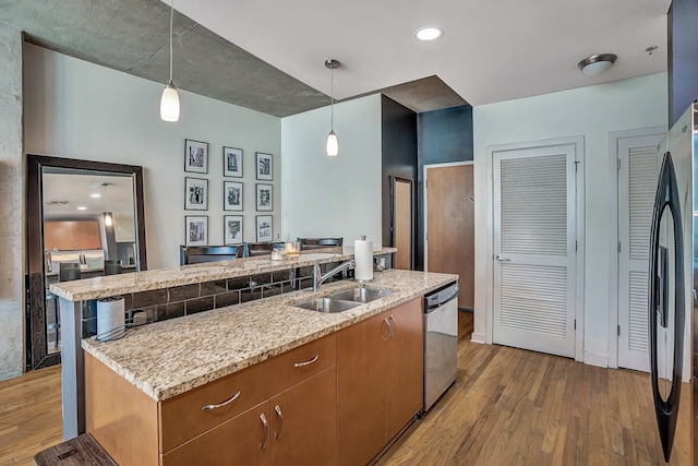 kitchen featuring brown cabinetry, light stone countertops, a sink, stainless steel appliances, and light wood-type flooring