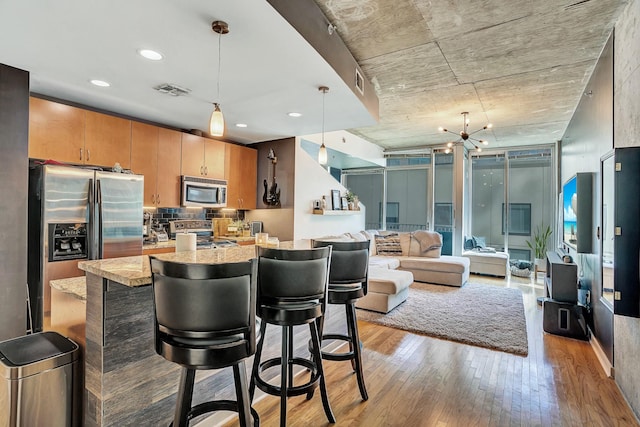 kitchen featuring visible vents, light wood finished floors, a breakfast bar, appliances with stainless steel finishes, and decorative light fixtures