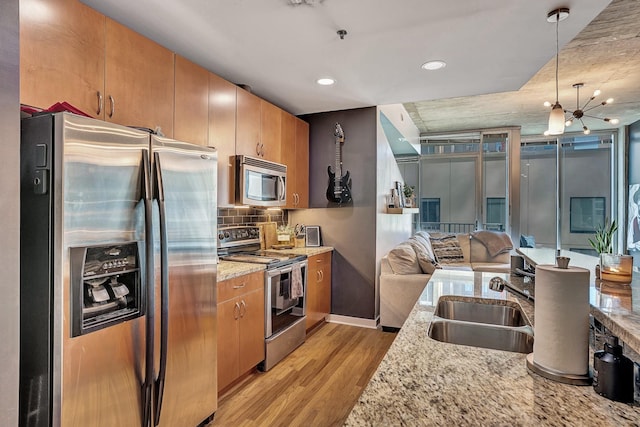 kitchen with a sink, light wood-style floors, appliances with stainless steel finishes, open floor plan, and backsplash