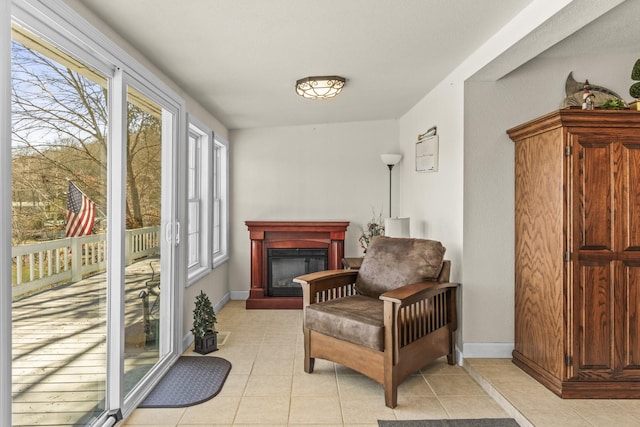 living area with light tile patterned flooring, a glass covered fireplace, and baseboards