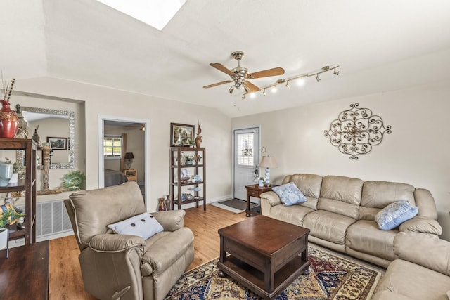 living room featuring ceiling fan, baseboards, lofted ceiling with skylight, and wood finished floors