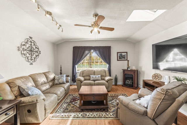 living room featuring ceiling fan, vaulted ceiling with skylight, a textured ceiling, and wood finished floors