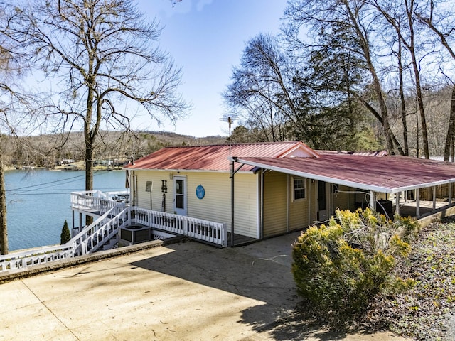 view of property exterior featuring central AC unit, driveway, metal roof, and a water view