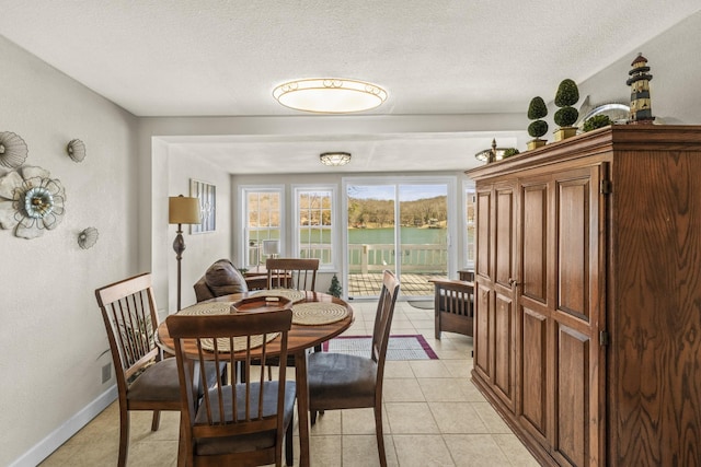 dining area featuring light tile patterned flooring, a textured ceiling, baseboards, and a water view