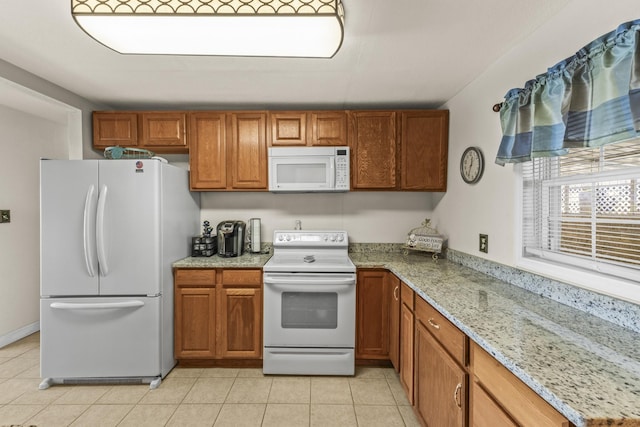 kitchen featuring light tile patterned floors, brown cabinets, white appliances, and light stone counters