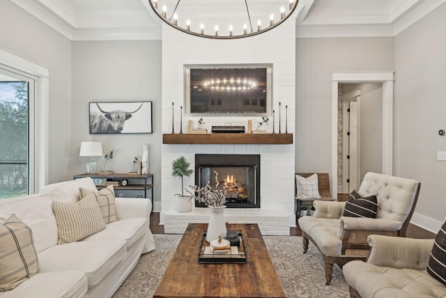 living room with a notable chandelier, wood finished floors, a fireplace, and crown molding