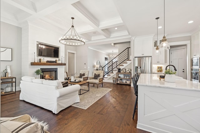 living room featuring stairway, coffered ceiling, a lit fireplace, dark wood-type flooring, and a notable chandelier