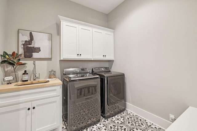 clothes washing area with independent washer and dryer, a sink, cabinet space, light tile patterned flooring, and baseboards