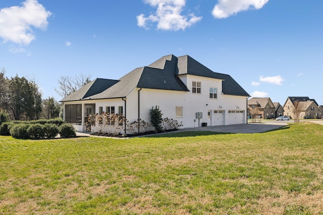 rear view of property with aphalt driveway, a yard, a garage, and a sunroom