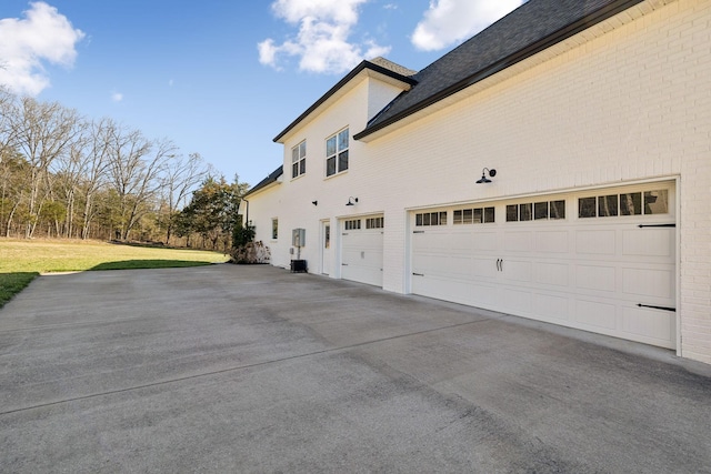 view of home's exterior with brick siding, a garage, a yard, and driveway