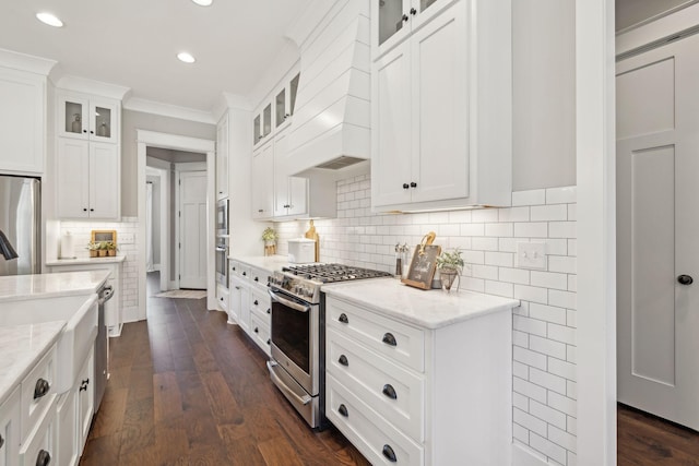 kitchen featuring ornamental molding, white cabinetry, appliances with stainless steel finishes, light stone countertops, and dark wood-style flooring