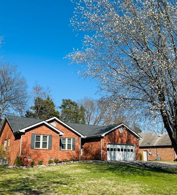 ranch-style house featuring brick siding, an attached garage, driveway, and a front yard