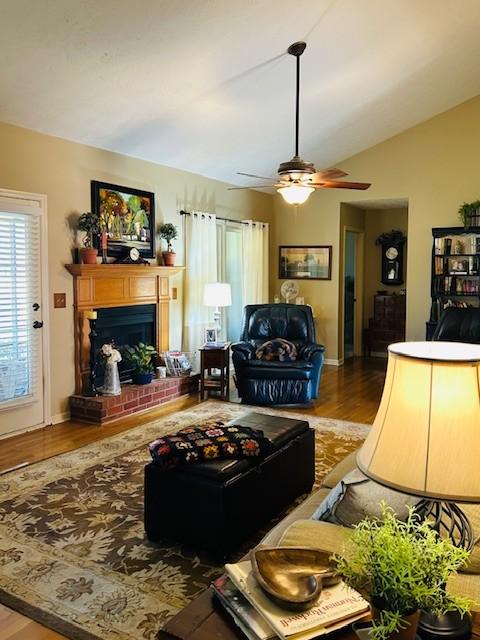 living area featuring a brick fireplace, baseboards, lofted ceiling, wood finished floors, and a ceiling fan