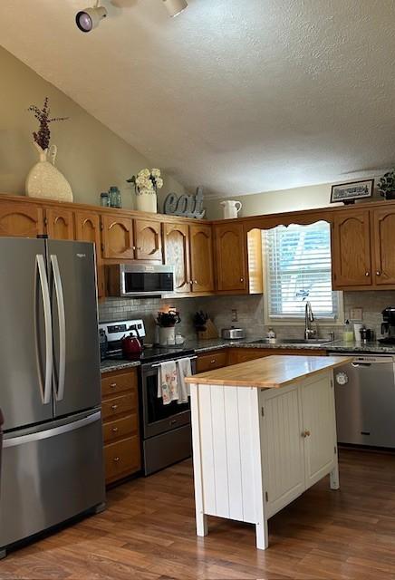 kitchen featuring a sink, a center island, stainless steel appliances, dark wood-style flooring, and vaulted ceiling