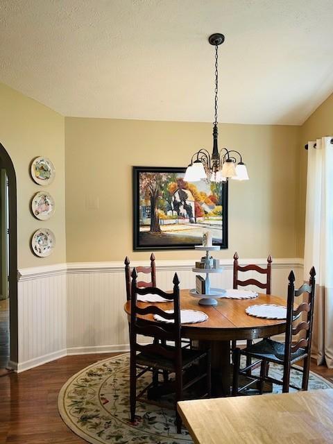 dining area with arched walkways, a notable chandelier, wainscoting, and wood finished floors