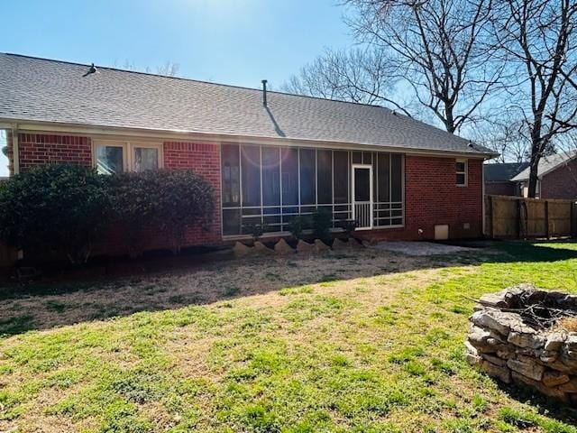 rear view of house with fence, a yard, roof with shingles, a sunroom, and brick siding