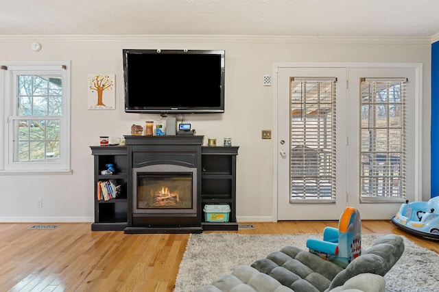living room featuring visible vents, ornamental molding, a glass covered fireplace, wood finished floors, and baseboards
