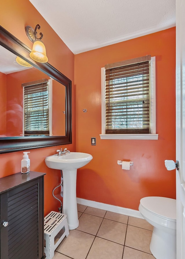 half bath with baseboards, a sink, tile patterned flooring, a textured ceiling, and toilet